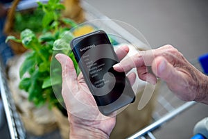 Unrecognizable senior couple man with smartphone doing shopping in supermarket.