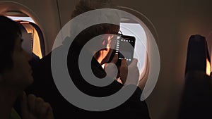 Unrecognizable senior male passenger taking smartphone photo of plane wing during flight sitting near airplane window.