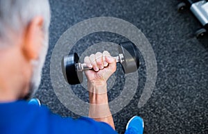 Unrecognizable senior man in gym working out with weights.