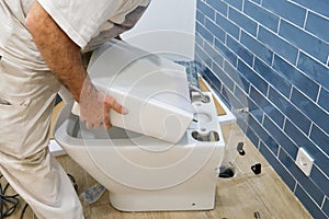 Unrecognizable senior plumber installer installing toilet cistern.