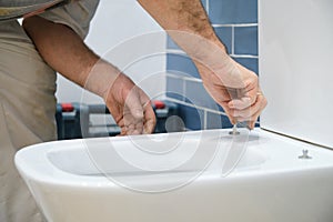 Unrecognizable senior plumber installer installing toilet lid.