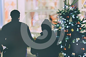 Unrecognizable silhouettes of people near shop window, Christmas tree with decorations. Christmas shoping