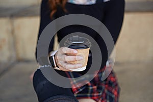 Unrecognizable skater girl wearing modern smart wrist watches and sitting in a skatepark with a cup of coffee in hand