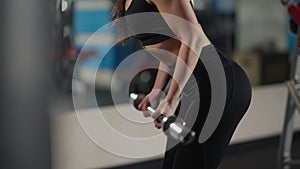 Unrecognizable slim sportswoman pulling up barbell to belly standing in gym indoors. Fit young endurant woman exercising