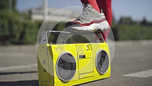 Unrecognizable slim woman in red legging and sneakers stomping on vintage yellow tape recorder. Unknown sportswoman with