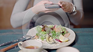 Unrecognizable slim woman taking photo of healthful dietary salad with vegetables and fish in restaurant. Young