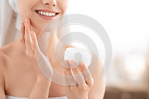 Unrecognizable smiling woman applying face cream, copy space