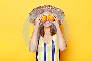 Unrecognizable smiling woman wearing striped swimming suit and sun hat isolated on yellow background hiding her eyes behind