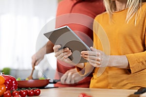 Unrecognizable spouses cooking healthy dinner, checking recipes online, using tablet