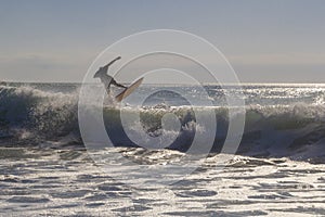 Unrecognizable surfer jumping over a wave, silhouetted against the sky at golden hour