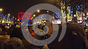 Unrecognizable tourists recording videos and shooting photos of New Year light show near famous triumphal arch, Arc de
