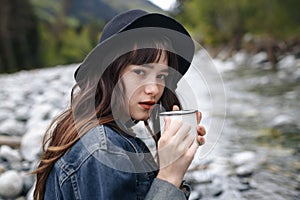 Unrecognizable Traveler Pouring Tea Or Coffee To Cup From Thermos On Waterfall Background. Tourism And Travel Concept