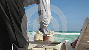 An unrecognizable waiter bringing coconut cocktails for relaxing young man by the sea. 3840x2160