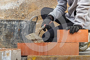 Unrecognizable woman bricklayering a wall in a costruction site with a trowel