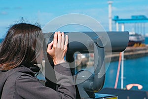 Unrecognizable woman brunette looks through binoculars at the sea.