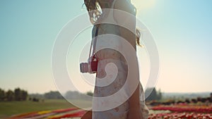 Unrecognizable woman with camera looking back at garden with spring flowers.