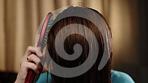 An unrecognizable woman is combing her wet hair with a comb. Close-up. Hair care. Dark background