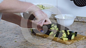 Unrecognizable woman cut cucumber on cutting board on kitchen table. Hands closeup. Front view.