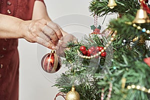 Unrecognizable woman decorating a Christmas tree, hanging a bell on a branch