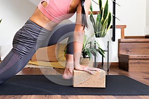 Unrecognizable woman doing yoga twist at home with help of cork yoga block.