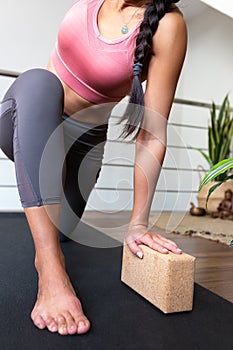 Unrecognizable woman doing yoga twist at home with help of cork yoga block. Vertical image.