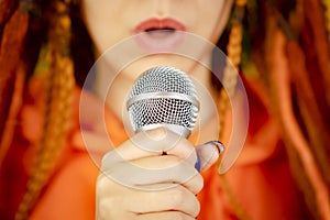 Unrecognizable woman with dreadlocks singing into microphone. Full frame. Body part of female with mic. Selective focus