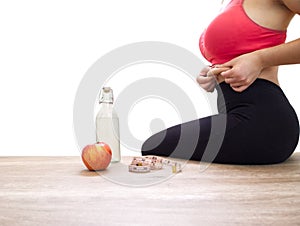 Unrecognizable woman grabbing her love handles on white background with measuring tape, an apple and a bottle of water