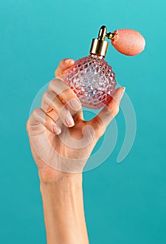 Unrecognizable woman hand showing classic perfume bottle against blue backdrop