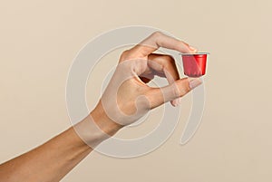 Unrecognizable woman hand showing coffee capsule against beige backdrop