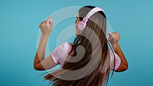 Unrecognizable woman with headphones dancing with her back to camera on blue background. Girl with long hair. Party