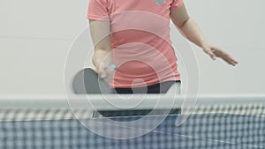 Unrecognizable woman hitting ball with racket over table tennis net. Young Caucasian sportswoman training ping-pong in