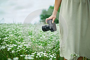 Unrecognizable woman hold digital camera in her hands on flower field landscape