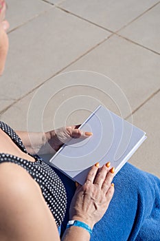 unrecognizable woman holding blank book for mockup design, sitting by the swimming pool