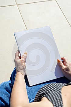 unrecognizable woman holding blank magazine for mockup design, sitting by the swimming pool