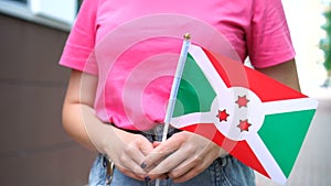 Unrecognizable woman holding Burundian flag. Girl walking down street with national flag of Burundi