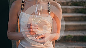 Unrecognizable woman holding champagne relaxing under evening sunlight outdoors.