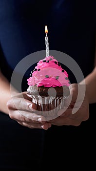 unrecognizable woman holding a chocolate cupcake with a candle on her birthday