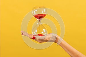 Unrecognizable woman holding hourglass in hand against yellow backdrop