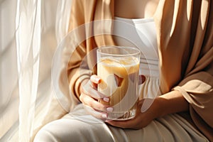 unrecognizable woman holding iced coffee in glass, beige tones, natural light. AI Generated