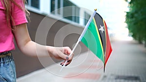 Unrecognizable woman holding Kittitian or Nevisian flag. Girl walking down street with national flag of Saint Kitts and