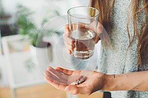 Unrecognizable woman holding supplement pills in one hand and a glass of water in other