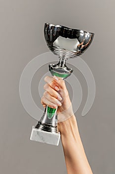 Unrecognizable woman holding trophy in hand against gray backdrop