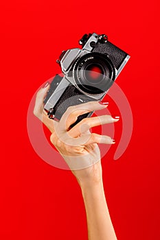 Unrecognizable woman holding vintage reflex photo camera against red backdrop