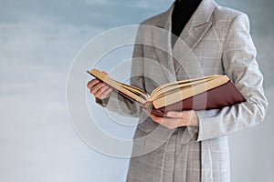 An unrecognizable woman holds a large brown book in her hands. business style, university teacher