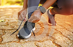 Unrecognizable woman lacing running shoes, smartwatch on wrist outdoors