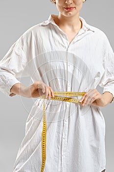 Unrecognizable woman measuring waist with sewing meter