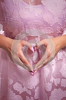 Unrecognizable woman in pink puffy dress makes with her hands a heart sign of love. Pink manicure. Medium close up shot