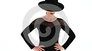 Unrecognizable woman posing with black hat on eyes, white studio background. Femme fatale, stylish outfit of ballet