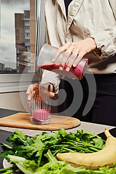 Unrecognizable woman pouring banana and black currant smoothie in glass
