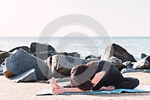 unrecognizable woman practicing yoga in Janu Sirsasana on beach